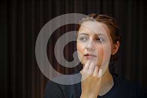 pensive young woman thinking hand on chin on dark background