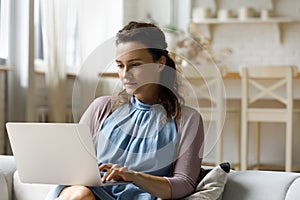 Pensive young woman using computer sitting on couch.