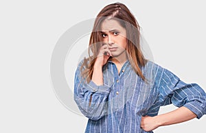 Pensive young woman wearing denim blue shirt, with finger folded on the mouth frowning her face and looking to the camera on white