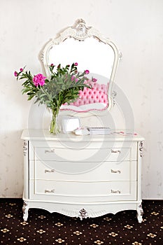 Peony flowers on a white commode under a mirror