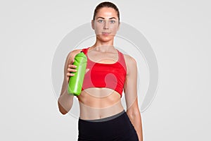 People, active lifestyle concept. Fatigue sportswoman feels thirsty after morning workout, holds green bottle with water, dressed