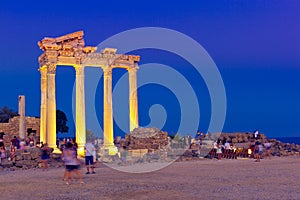People admire the beauty of colonnade of antique Temple of Apollo at sunset
