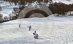 People of all ages sledging down a small Snow covered Hill in Glen esk, high up in the Angus Glens.