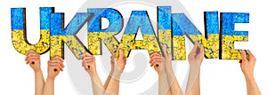 People arms hands holding up wooden letter lettering forming word UKRAINE in ukrainian national flag colors  blue and yellow. war