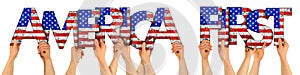 People arms hands holding up wooden letter lettering forming words maerica first with USA stars spangled banner national flag photo