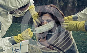 People in bacteriological protective suits putting a mask on woman