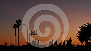 People on basketball court playing basket ball game. Sunset on beach, California photo