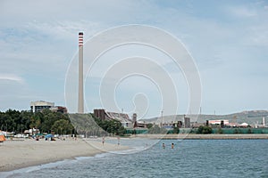 People bathing in a beach located next to a polluting industrial refinery