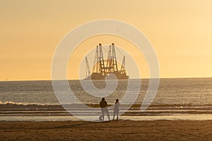 People at beach looking at industrial barge off Dutch coast