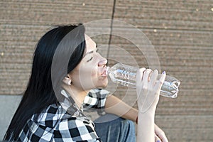 People. A beautiful Caucasian woman sits on the street near the wall and drinks water from a transparent bottle.