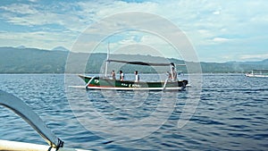 People on a boat sail behind the Stenellalongirostris family of dolphins that jump out of the water in the open, clear sea on the