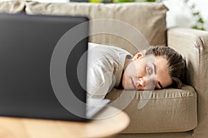Bored woman with laptop lying on sofa at home photo