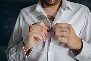 People, business, fashion and clothing concept - close up of man dressing up and fastening buttons on shirt at home