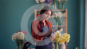 people, business and floristry concept. Portrait of happy smiling florist woman making notes to clipboard at her flower