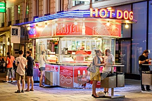 People Buying Hot-Dogs At Wurstel Hot Dog Stand On Graben Street In The Night
