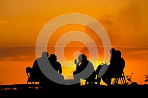 People in camping sitting near campfire against sunset