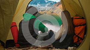 People on campsite traveling and hiking, exploring nature. Young loving couple sitting inside the tent at lake coast in