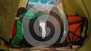 People on campsite traveling and hiking, exploring nature. Young loving couple sitting inside the tent at lake coast in