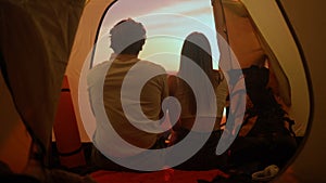 People on campsite traveling and hiking, exploring nature. Young loving couple sitting inside the tent looking at sunset