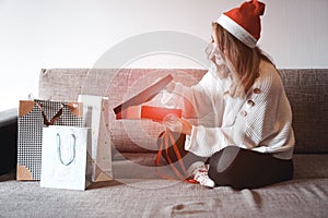 Beauty girl opening present gifts sitting on sofa at home