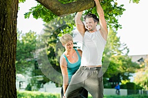 People in city park doing chins or pull ups on tree