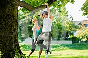 People in city park doing chins or pull ups on tree