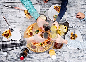 People clanging glasses together having pizza