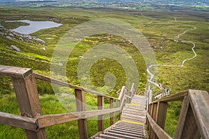 People climbing on steep steps and stairs of wooden boardwalk, to reach Cuilcagh Mountain peak