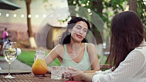 People, communication and friendship concept - smiling young women drinking orange juice and talking at outdoor cafe