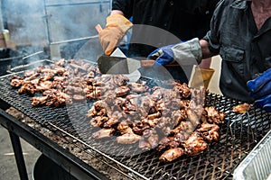 People cooking chicken wings and legs on barbecue grill street food outdoors festival