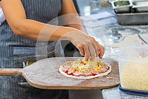 People and cooking concept - cook hand adding grated cheese to pizza
