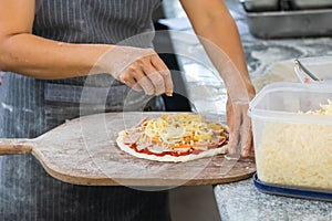 people and cooking concept - cook hand adding grated cheese to pizza
