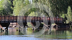 People Crossing River Bridge On Summer Day