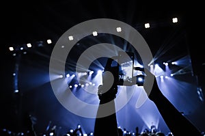 People in the crowd at a concert make video recordings and pics