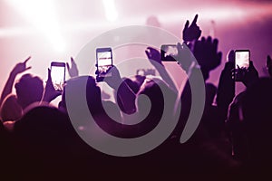 people from the crowd at a music festival in front of the stage are shooting videos and photos on their smartphones. The atmospher