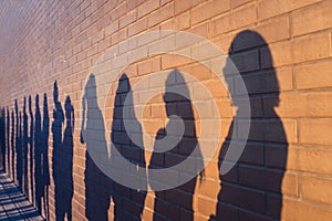 People crowd shadows lined up against a red brick wall. They are in a queue for changes in life. Social distance, covid