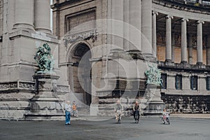 People cycle past the base of Triumphal Arch in Parc du Cinquantenaire, Brussels, Belgium