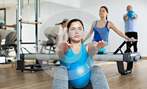 People of different ages pressing core and clutching mini Pilates balls between legs during Pilates training together