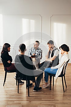 People of different ages sits in a circle during a meeting with a professional therapist