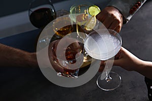 People with different alcohol drinks clinking glasses indoors, closeup