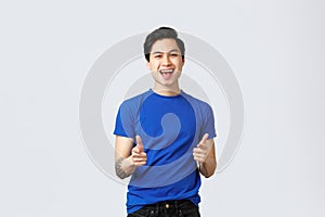 People different emotions, lifestyle and casual concept. Cheerful upbeat asian man in blue t-shirt, pointing fingers up