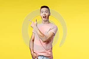 People, different emotions and lifestyle concept. Excited, happy asian man in pink t-shirt showing way, pointing finger