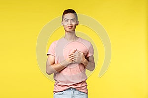 People, different emotions and lifestyle concept. Smiling touched asian man with stylish haircut, pink t-shirt, hold