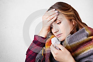 People, disease, healthcare concept. Stressful woman has flu, suffers from running nose, bad cold and headache, wrapped in wool pl