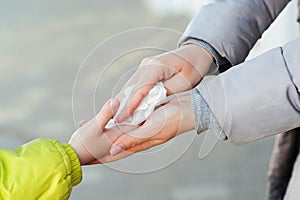 People disinfecting hands with antiseptic wet wipe outdoors. Woman cleaning kid hands with antiseptic tissue outdoors