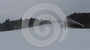 People do skiing on the mountainside. Skiers go down the snow slope. Out of focus background is the mountain slope with the descen