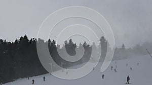 People do skiing on the mountainside. Skiers go down the snow slope. Out of focus background is the mountain slope with the descen