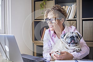 People and dog love friendship together - adult pretty young woman work at laptop computer and hug her adorable pug - happy female