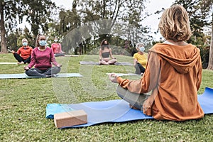 People doing yoga class while wearing safety masks at city park - Focus on teacher back