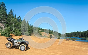 People driving ATV quads on sand beach of Foyross Lake. Foy, Sudbury, Ontario, Canada.